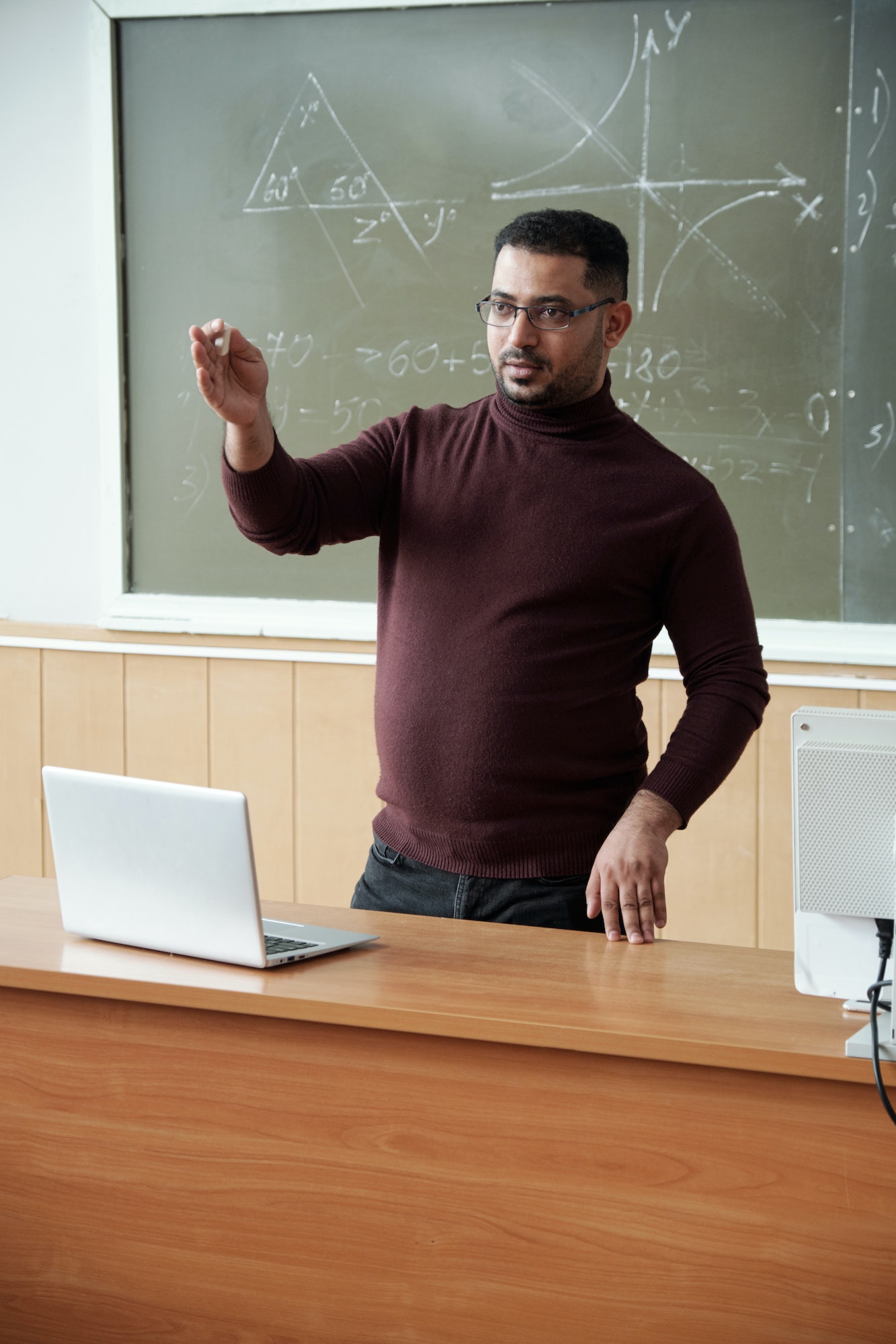 Mixed-race male in casualwear holding piece of chalk while explaining something to students